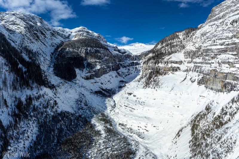 Aerial view up canyon from farther down canyon than the cabin.  Kirwan Cabin is in the shade between the two patches of trees upstream of the large avalanche path on the left.